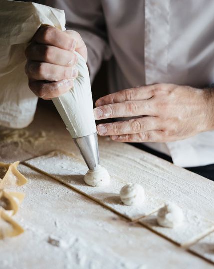 Ein Koch füllt frische Pasta mit Ricotta-Creme aus einem Spritzbeutel