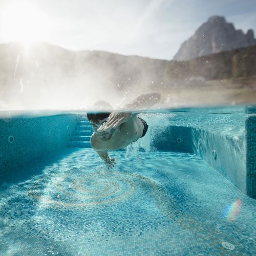 Un uomo che nuota sott'acqua nella nostra piscina esterna con vista sulle montagne