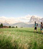 Ein Mann und eine Frau wandern entlang einer Almwiese, im Hntergrund die Dolomiten